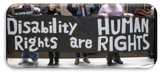 Disability Rights are Human Rights
A group of diverse protesters hold a long black sign that has the slogan 'Disability Rights are Human Rights' in white letters. 